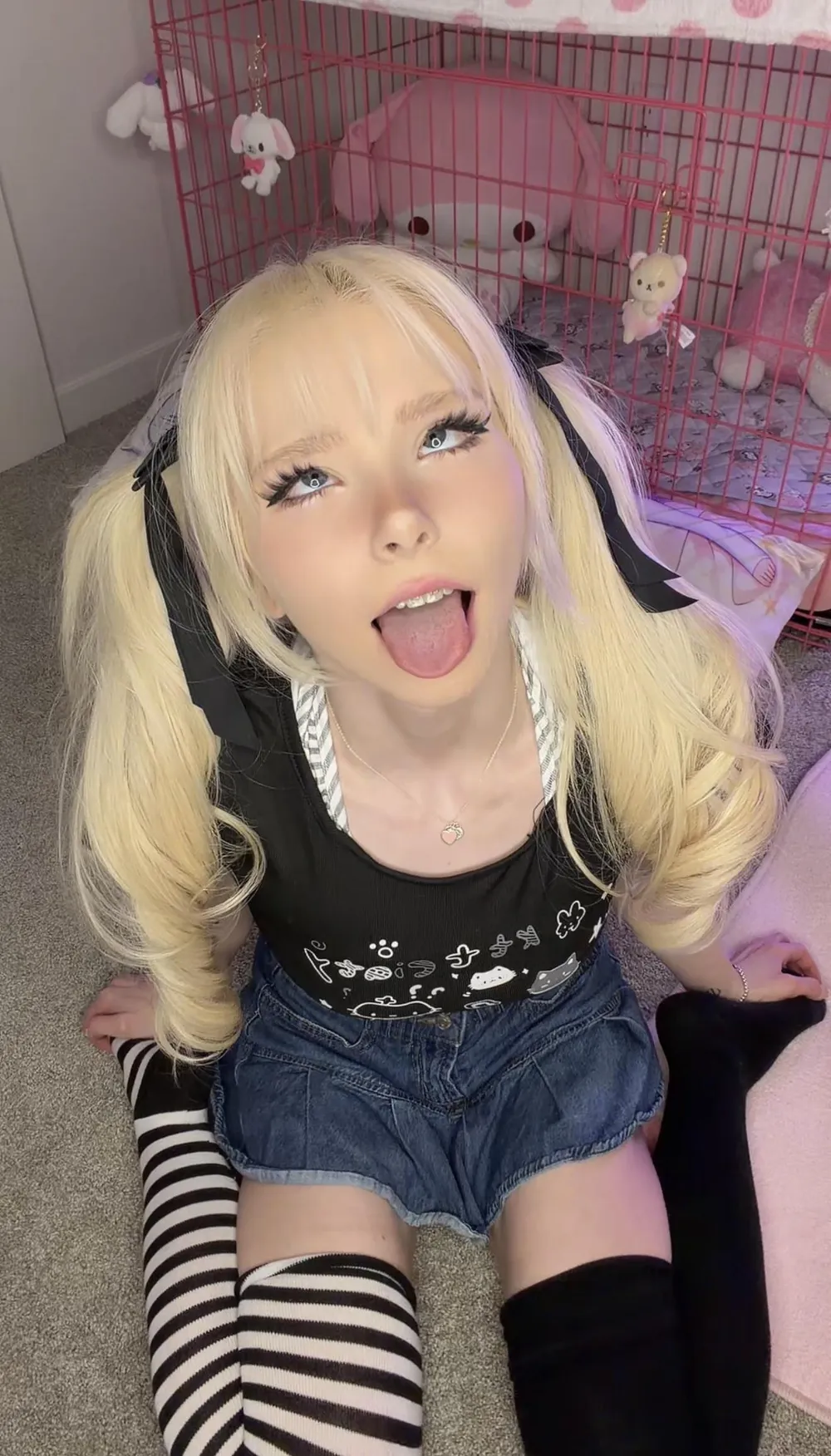 Mennah posing in a playful cosplay-inspired outfit with blonde pigtails and striped thigh-high socks
